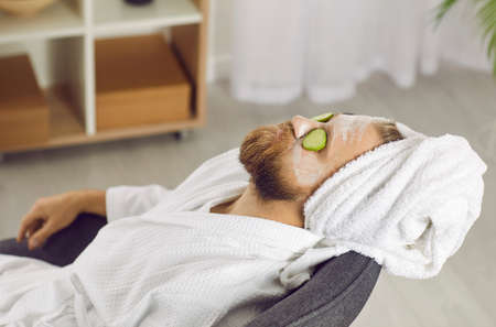 Metrosexual man in bathrobe make beauty face skin procedures for glowing healthy look. Calm guy relax on spay day at home, do cosmetic facial treatment or mask. Male skincare and cosmetology.の写真素材