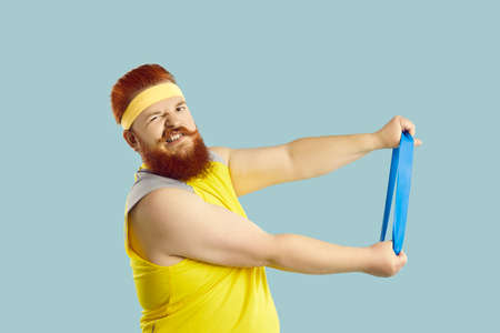 Funny fat guy trying to do fitness exercise with elastic band. Studio shot of large, big, stout man...