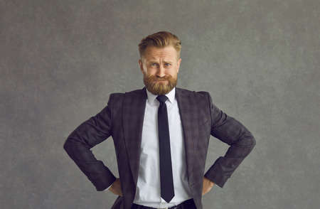 Portrait of an anxious and tense businessman expecting something while standing on a gray background. Man with a frowning face holds his hands to his sides. Concept of emotions and facial expressions.の写真素材