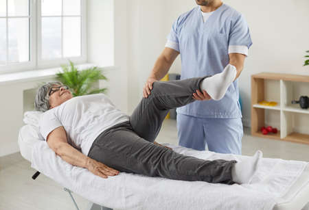 Happy senior woman lying on exam couch while chiropractor, osteopath or physiotherapy specialist is...