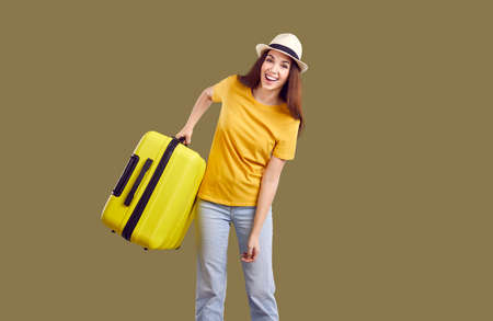 Overjoyed millennial Caucasian girl in casual summer clothes hold suitcase excited about travel or vacation. Funny young woman isolated green studio background ready for summertime holidays.の写真素材