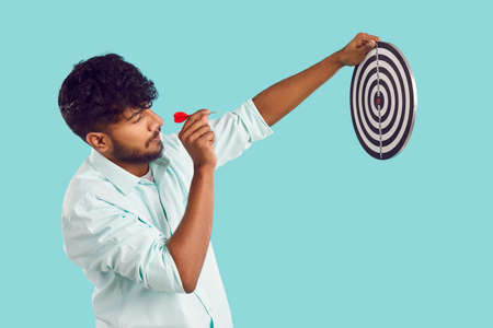 Indian man shooting at target. Profile view of young South Asian man in shirt standing isolated on...