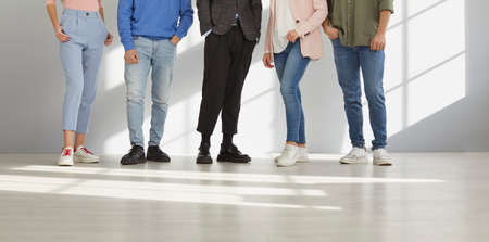 Cropped shot of the legs of young unrecognizable stylish people in smart casual clothes people who are standing in a row. Variety of stylish young people stand in bright spacious room with sunlight.の写真素材