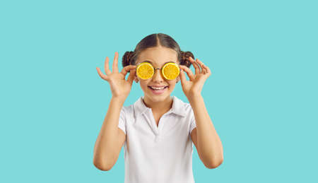Funny little preteen girl in summer glasses in shape of orange slices on turquoise background. Portrait of cute cheerful little girl with hairstyle with two bundles having fun during summer vacation.の写真素材