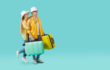 Happy couple going on romantic holiday trip. Young millennial man and woman in casual yellow shirts, summer hats and sun glasses looking to side at empty blue copyspace background. Travelling conceptの写真素材