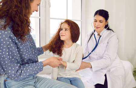 Female doctor puts stethoscope to childs back and listens to breathing and lungs of little girl who...