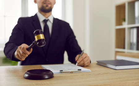 Judge in formal suit sitting at his table, giving judgment at the end of trial session, and hitting...