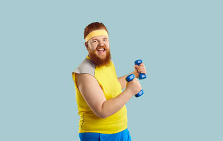 Funny happy excited bearded redhead plump fat man in yellow top and sweatband having fun while doing...