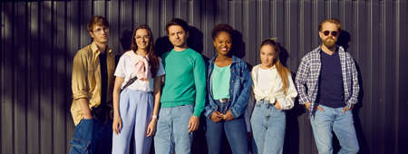 Handsome men and beautiful women in modern comfortable everyday clothes. Group portrait of six diverse relaxed young people in shirts, tees and jumpers leaning on street wall. Casual fashion conceptの写真素材
