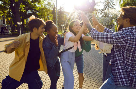 Bunch of happy young people give high five to their friend. Cheerful joyful diverse friends spending...