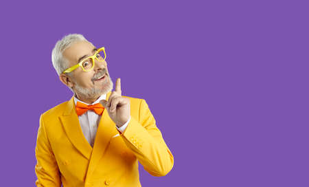 Middle aged man with a beard in a yellow jacket, bow tie and glasses is amazed and surprised,...