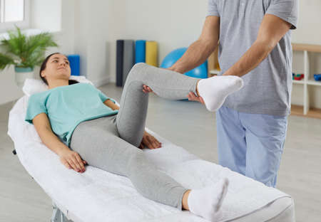 Physiotherapist work with patient leg injury or trauma help with pain relief. Male therapist do exercises with female client do rehabilitation for fast recovery. Rehab and physiotherapy concept.の写真素材