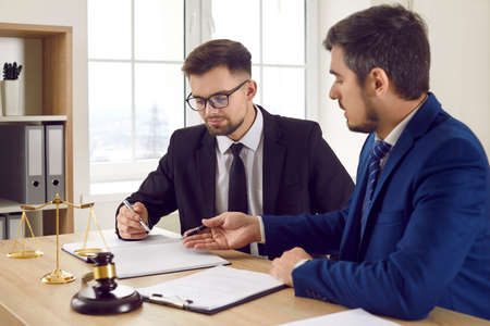 Two professional male lawyers read legal documents and study information about court case together....