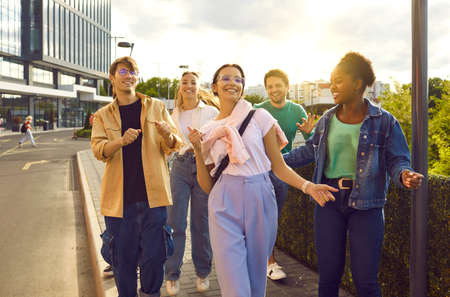 Group of fun and cool friends hang out together walking streets in summer on weekend. Multiracial men and women in casual clothes have fun walking on sidewalk against backdrop of city buildings.の写真素材