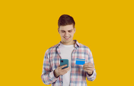 Happy guy with mobile phone and credit card makes online purchases using banks mobile application....