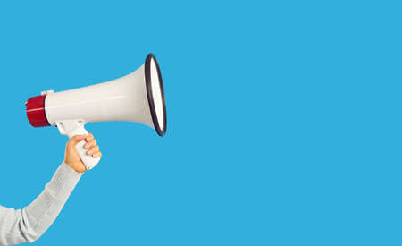 Hand with megaphone isolated on blue studio background making announcement. Person with loudspeaker attract attention for sale or offer. Advertising and promotion. Copy space.の写真素材