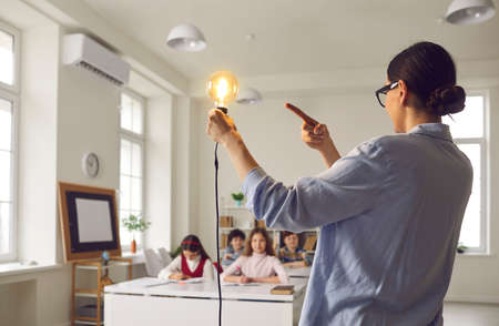 School science teacher shows students shining light bulb. Female teacher holding Edison lightbulb telling happy junior schoolkids about electricity. Concept of education and creative ideas in classの写真素材