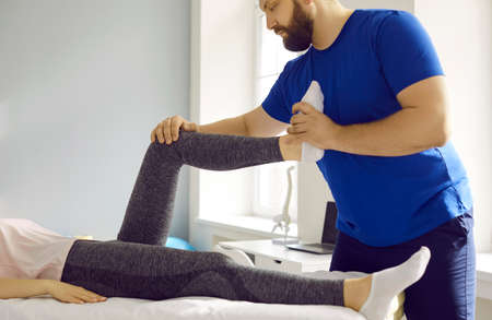Pprofessional male masseur therapist kneads female patients leg in physiotherapy clinic. Cropped...