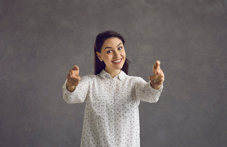 Positive carefree woman makes finger pistols pointing straight at the camera saying I choose you....