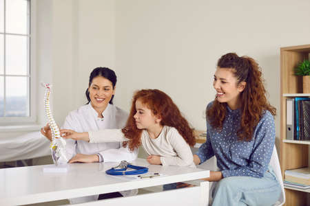 Curious kid together with mum visits doctor and learns about human skeleton. Happy woman and her...