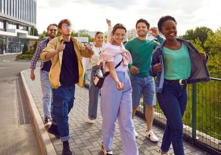 Group of multiracial friends are having fun walking along sidewalk on city street. Cool and stylish...