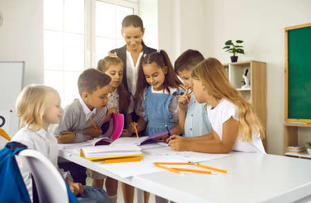 Happy teacher and students having interesting class. Group of school children standing at table in...