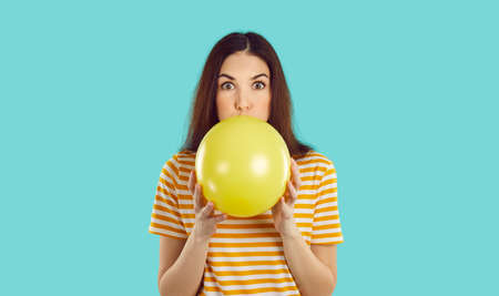 Woman blowing up birthday party balloon. Young brunette girl in striped orange white tee shirt...