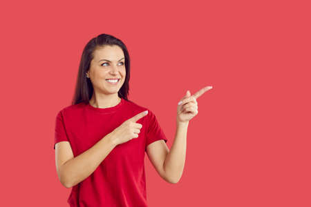 Smiling woman isolated on red studio background point with fingers at good sale deal or offer. Happy...