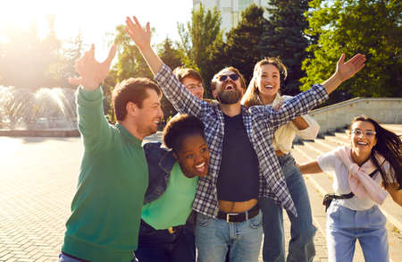 Cheerful group of friends have fun, rejoice, laugh and hug while walking streets of city. Happy...