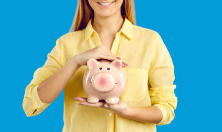 Crop close up happy woman isolated on blue studio background hold piggybank for money saving....