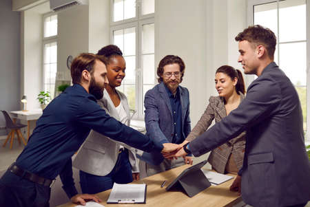 Cheerful business team in good mood together tunes in to workflow and productive work. Multiracial men and women in office form stack of hands to motivate before starting project. Concept of teamwork.の写真素材