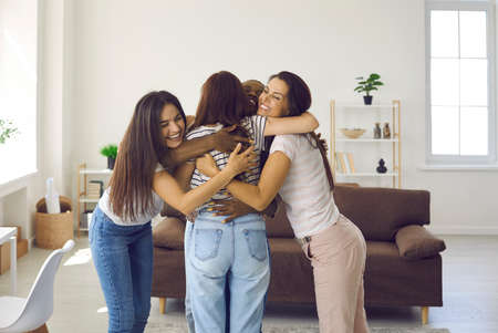 You did it, girl. Diverse group of happy young women hugging friend and congratulating her on success. Joyful ladies greeting each other at get together, casual gathering at home, reunion meetingの写真素材