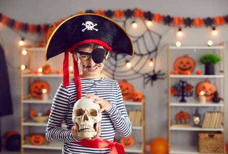 Portrait of smiling small boy kid child in costume hold skull celebrate school Halloween carnival. Happy child dressed for all saints eve fall scary party in kindergarten. Autumn holiday masquerade.の写真素材