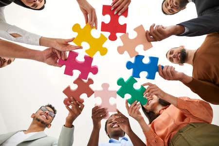 Diverse multiracial multi ethnic team of happy smiling adult men and women holding colorful jigsaw puzzle parts, bottom view, from below. Modern business, teamwork, education, innovative ideas conceptの写真素材