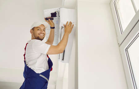 Technician service. Portrait of friendly male professional worker who installs new air conditioner in clients apartment. Smiling man is installing air conditioning equipment with screwdriver.の写真素材