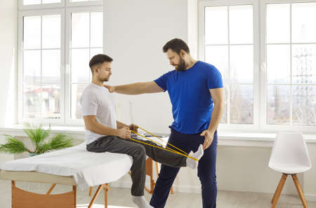 Physiotherapy and rehabilitation after sports injuries. Male physiotherapist assisting man to...