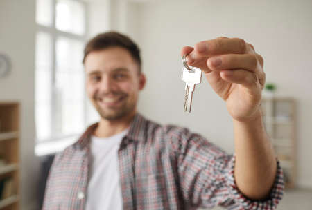 Happy owner holding and showing the key to his new home. Close up of house keys in the hand of a...