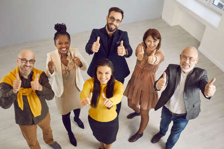 Multiracial team of business people showing thumbs up together. Group of happy multiethnic male and female colleagues looking up at camera, smiling and doing thumbs up gestures. Teamwork conceptの写真素材