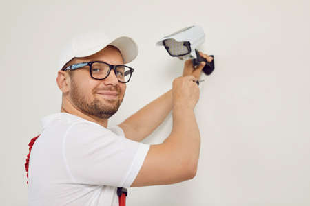 Portrait of smiling male technician worker who installing video surveillance camera. Young man in...
