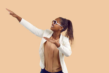 Cheerful african american woman having fun under moving and rhythmic music on beige background....