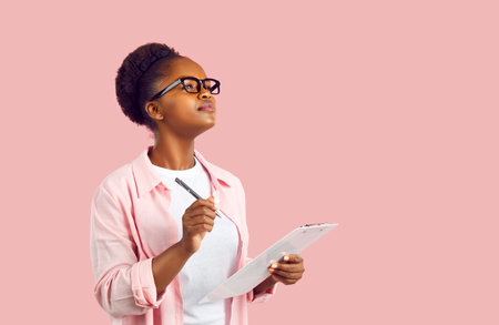 Attractive young African American woman student wearing glasses holds clipboard and pen to take...