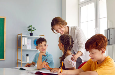 Lesson for kids at elementary school. Friendly smiling female teacher helping her little students...