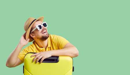 Wide narrow shot of funny smiling young man in summer hat and sunglasses with suitcases dream of vacation or trip. Happy male traveler imagine good holidays. Copy space. Travel and tourism concept.の写真素材