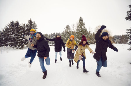 Overjoyed young people in outerwear have fun play snowballs in park together. Happy teen friends...