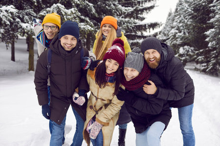 Portrait of happy diverse friends in outerwear relax on walk on winter holiday or vacation. Smiling young people in winterwear have fun enjoy weekend in snowy park or forest. Friendship concept.の写真素材