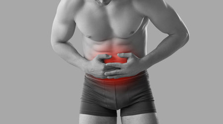 Crop black and white image of unwell young man in underwear on studio background suffer from belly ache. Pain in abdomen. Guy feel sick struggle with stomachache. Indigestion or intoxication.の写真素材