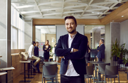 Portrait of positive millennial businessman posing against background of modern office. Friendly...
