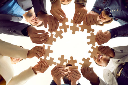 Diverse team of happy people connecting parts of a jigsaw puzzle. Multiracial group of men and women together make a circle from different wooden jigsaw parts. Business and teamwork concept backgroundの写真素材