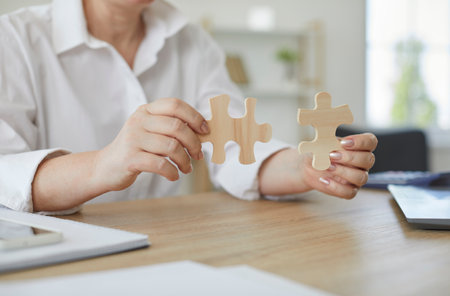 Senior woman at office desk connecting jigsaw puzzle parts. Businesswoman sitting at table and...