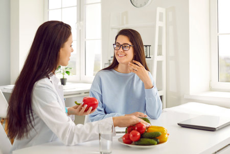 Dietitian helping woman lose weight. Nutritionist giving dieting consultation. Happy beautiful Caucasian girl listening to doctor recommending good dietary habits like natural food and balanced menuの写真素材